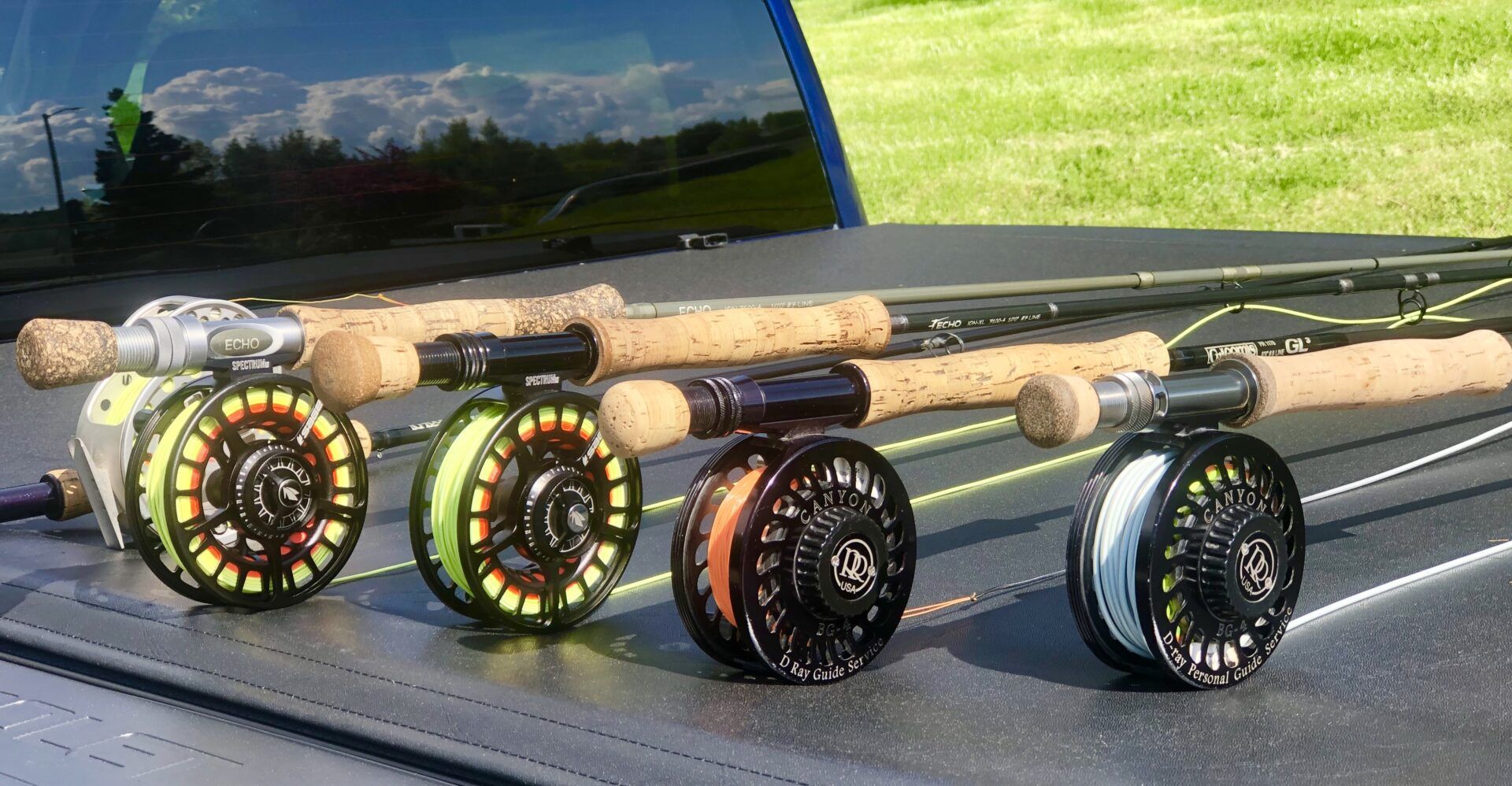 Four fly fishing rods with reels lined up on the bed of a pickup truck.