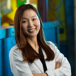 Portrait of a smiling professional in a white lab coat, arms crossed, in a colorful office setting
