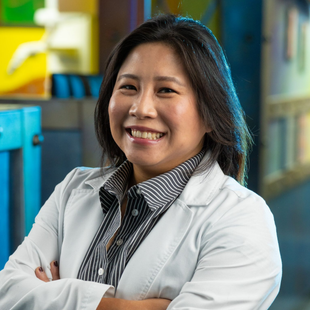 Smiling scientist in a lab coat with arms crossed in a colorful laboratory
