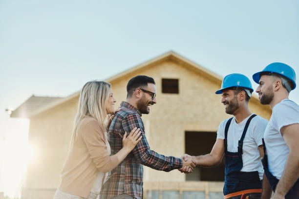 Happy couple greeting manual workers in front of renovating house