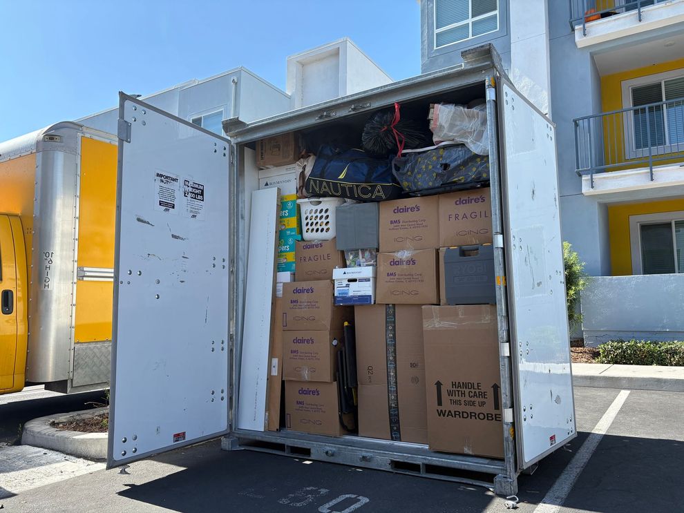 Open shipping container packed with cardboard boxes outside modern buildings