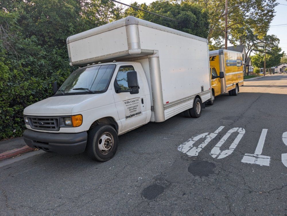 White box truck parked on a street with a yellow truck behind it and a stop marking on the road