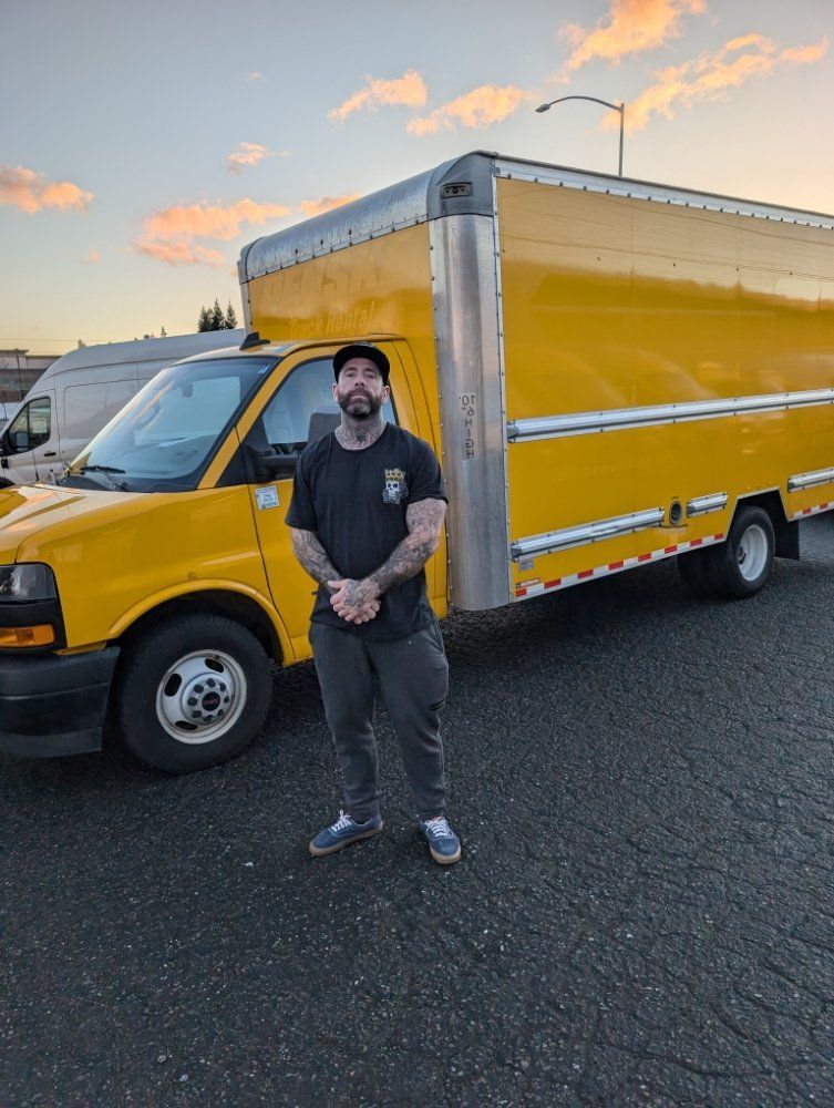 Man standing in front of a yellow box truck at sunset on a road
