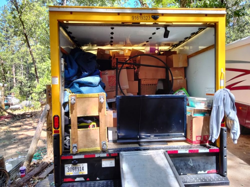 Open box truck packed with furniture, boxes, and a TV on the back.