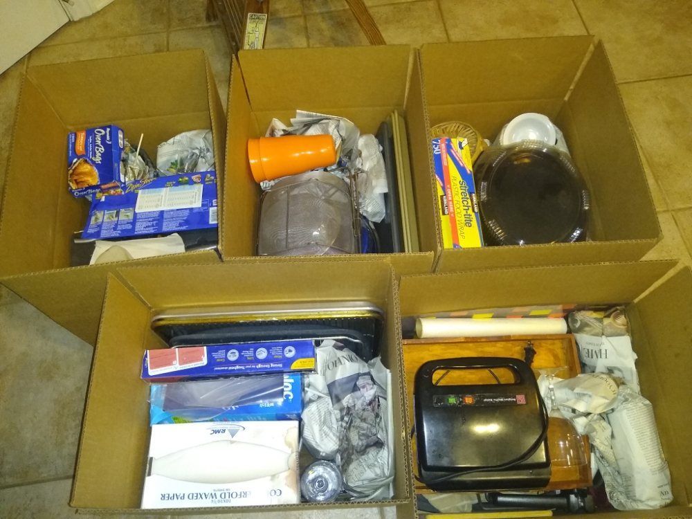 Open cardboard boxes filled with assorted household items and packaged goods on a floor.