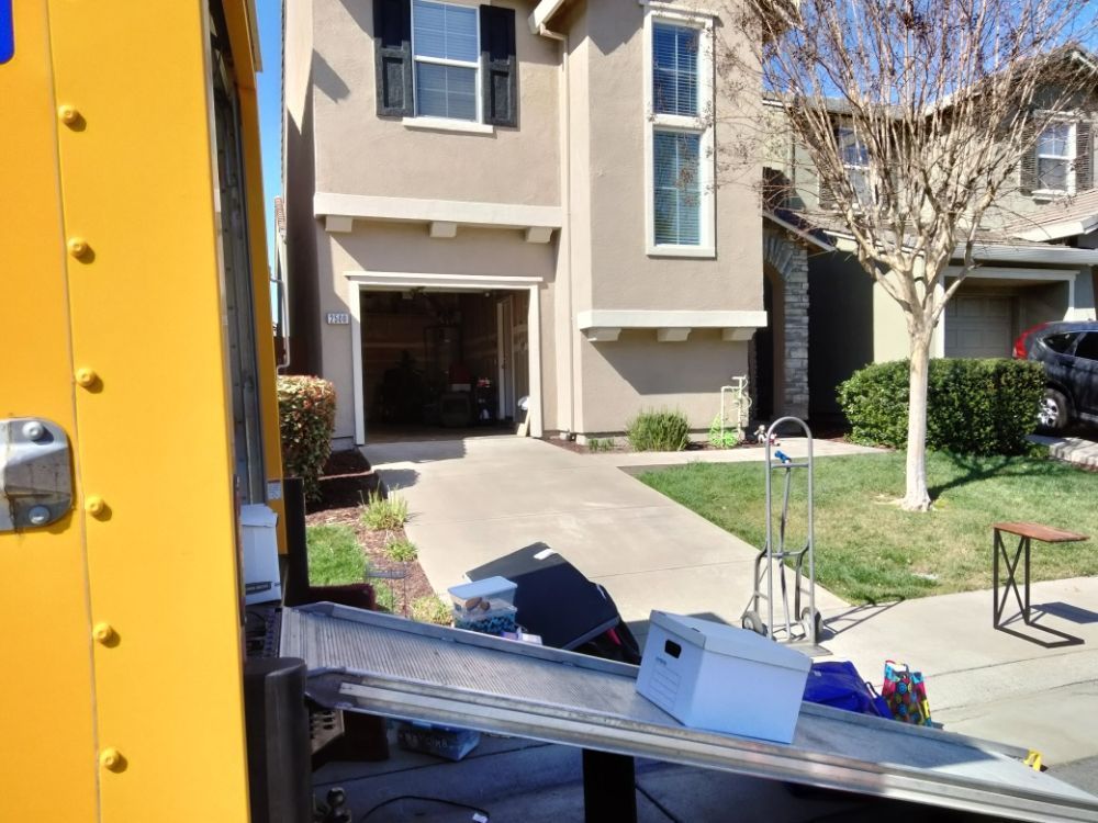 Yellow truck parked by a townhouse with a moving truck ramp extending into the driveway