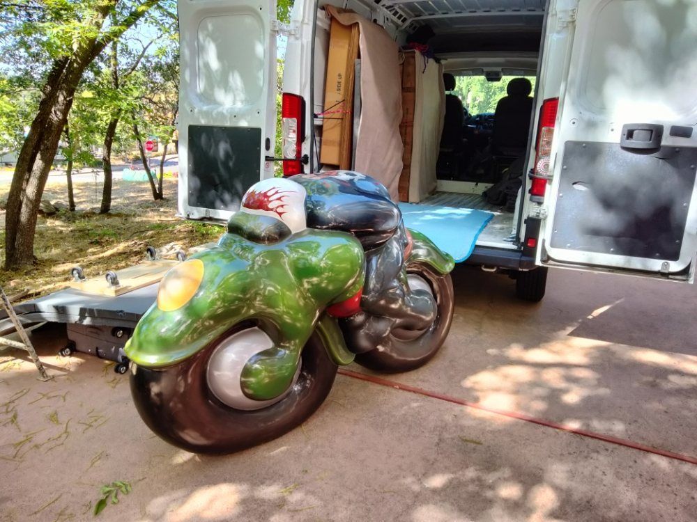 Green motorcycle parked at the back of an open white van in a sunny yard