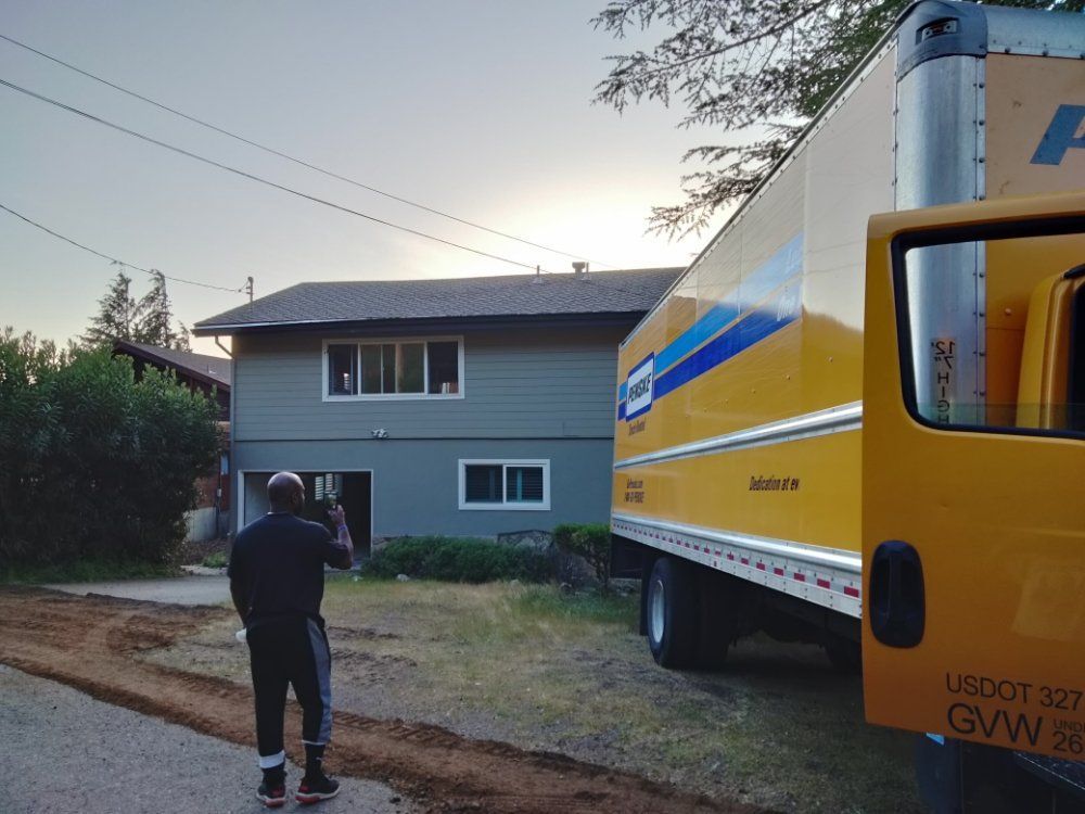 Person photographing a yellow moving truck parked beside a gray house at dusk