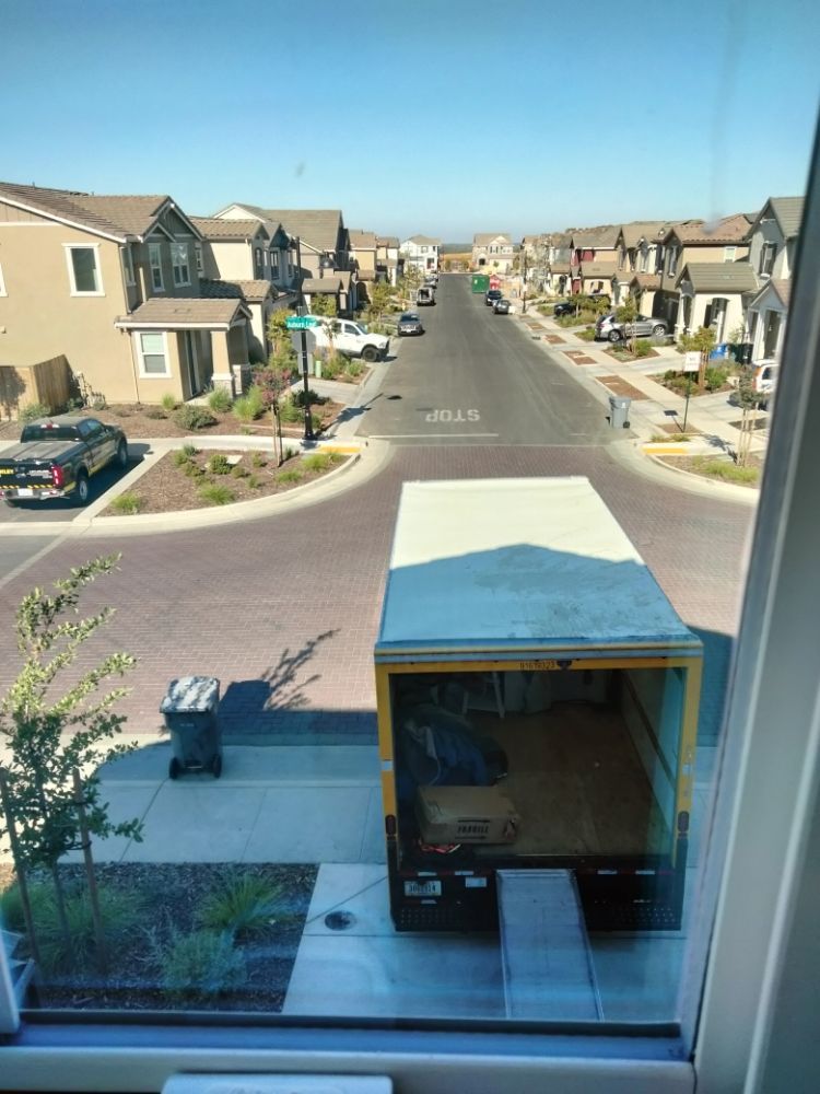 View from an upstairs window of a suburban street with houses and a moving truck parked below.