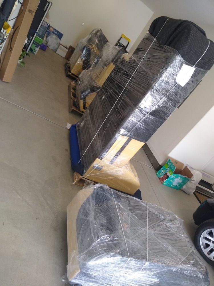 Wrapped furniture and boxes stacked in a garage-like storage area with a car partially visible.