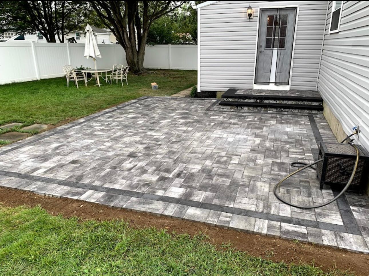 Completed grey paver patio with dark border and matching entrance steps in Terryville, NY