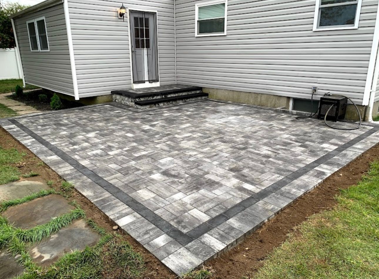 Wide view of a Terryville backyard patio with grey paving, dark perimeter border and matching stoop