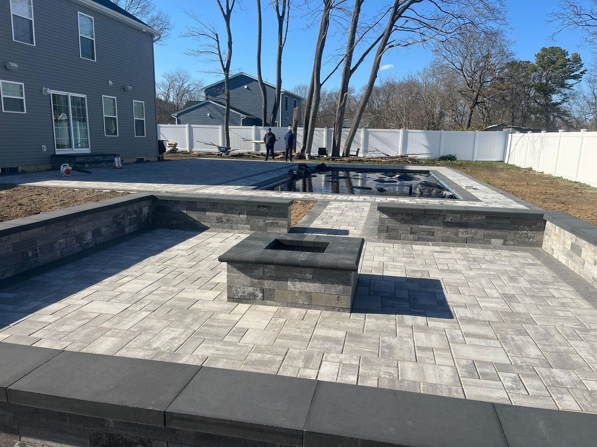 Grey paver patio with a square masonry firepit and low walls with dark caps