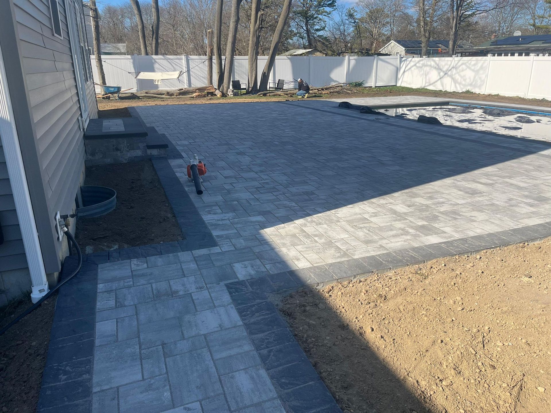 Grey paver patio beside a house with a connecting walkway and matching entrance steps
