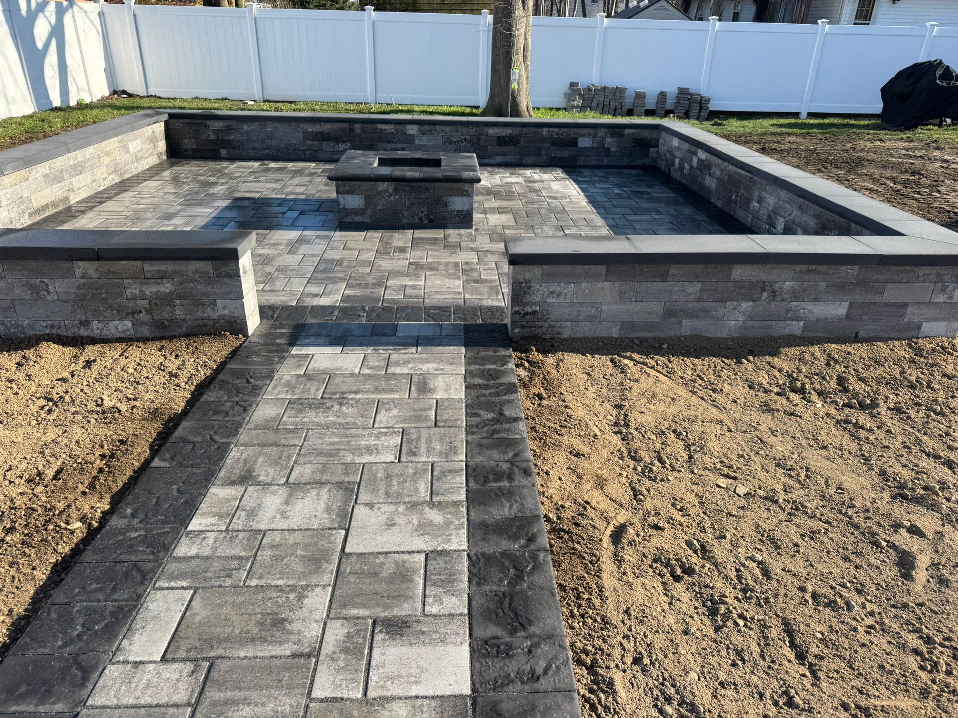 Paved firepit seating area enclosed by low masonry walls and approached by a bordered walkway