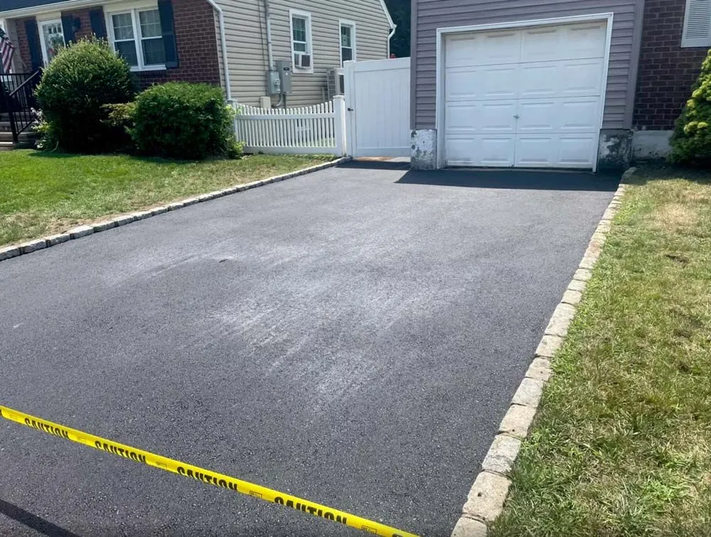 Black asphalt driveway leading to a garage with stone edging