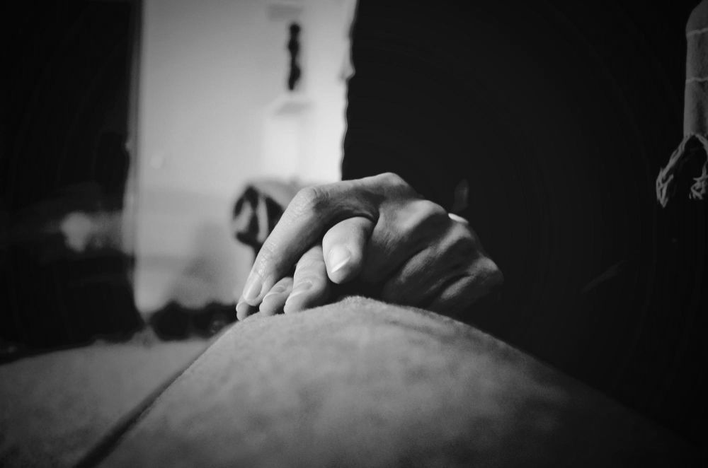 Hand resting on a bent knee in a dim, black-and-white scene