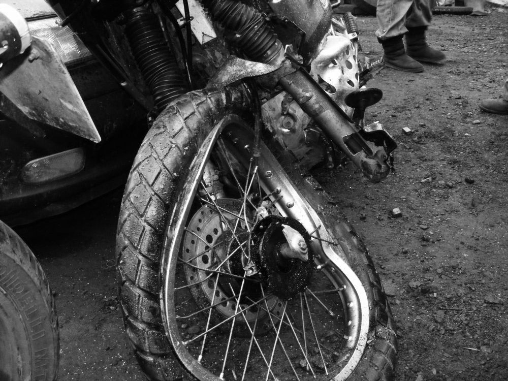 Damaged motorcycle front wheel after a crash, lying on a dirt road.