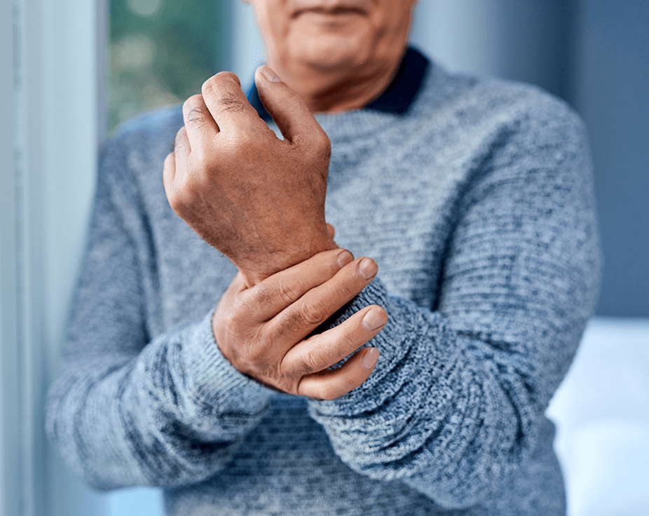 Person holding a painful wrist with one hand against a blue sweater, suggesting joint pain