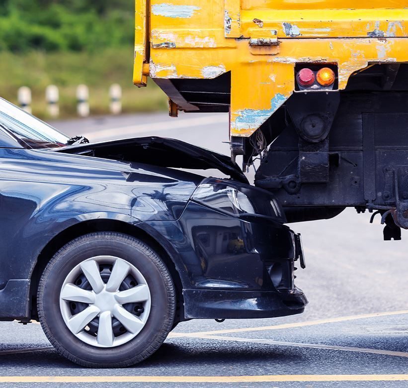Black sedan rear-ended by a yellow truck on a road, with visible front-end damage.