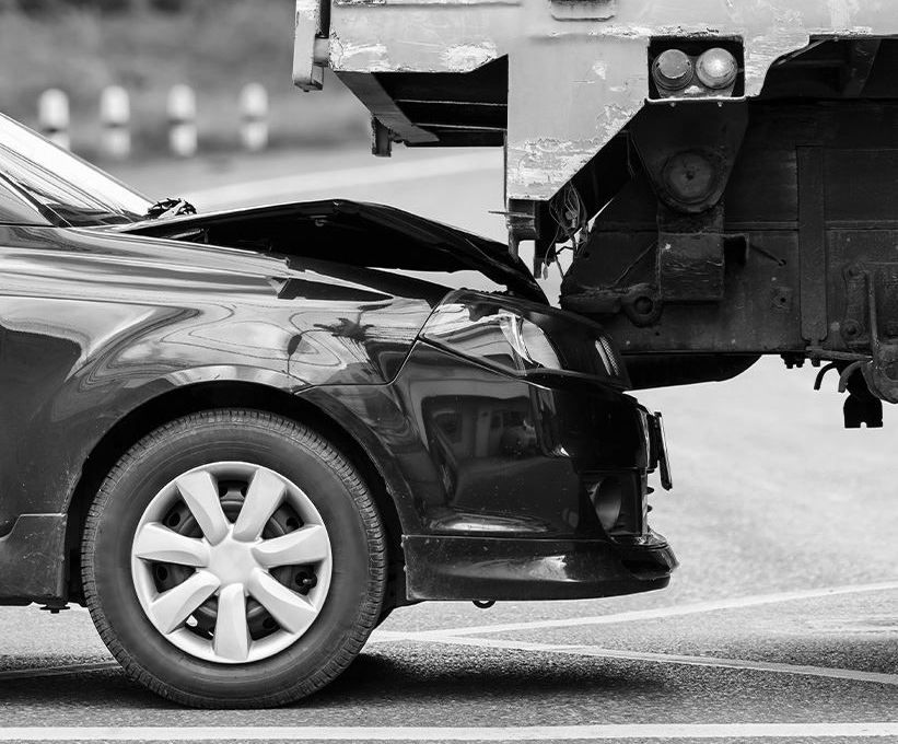Black car’s front end crushed under a truck in a collision on a road