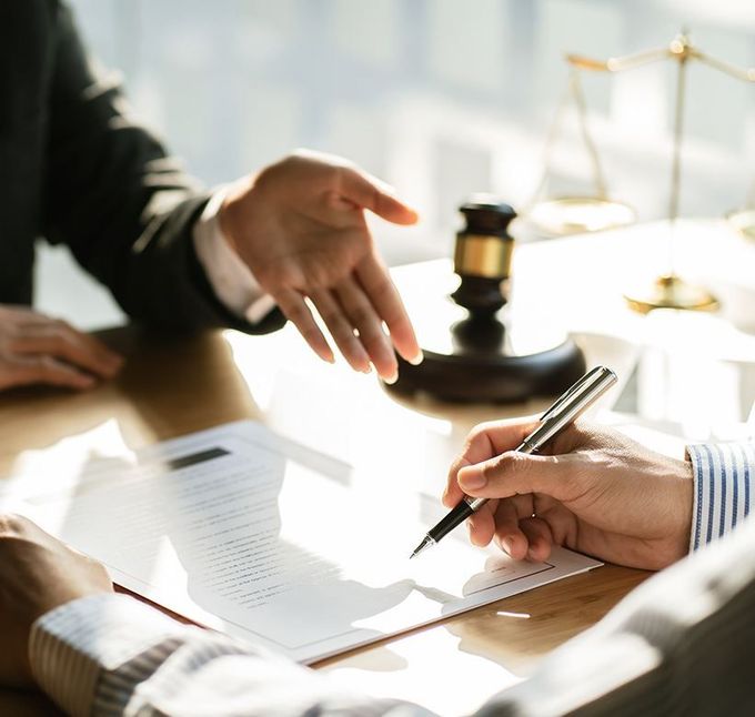 Hands signing a document at a sunlit office desk with a gavel and paperwork nearby
