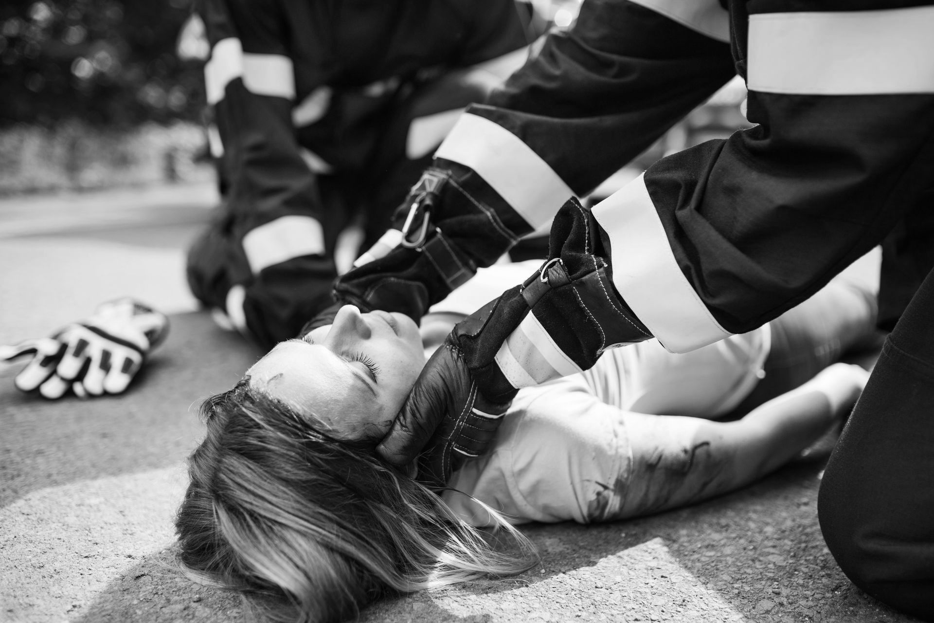 Paramedics kneel beside an injured person lying on the road, providing emergency care.