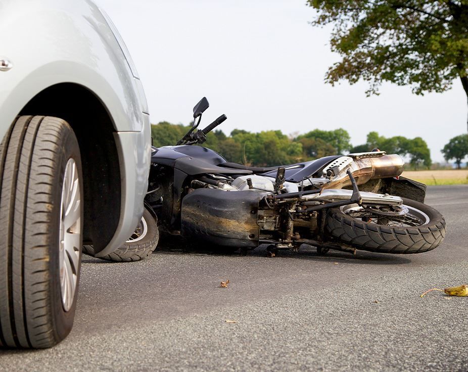 Damaged motorcycle lying on road beside a white car after a crash