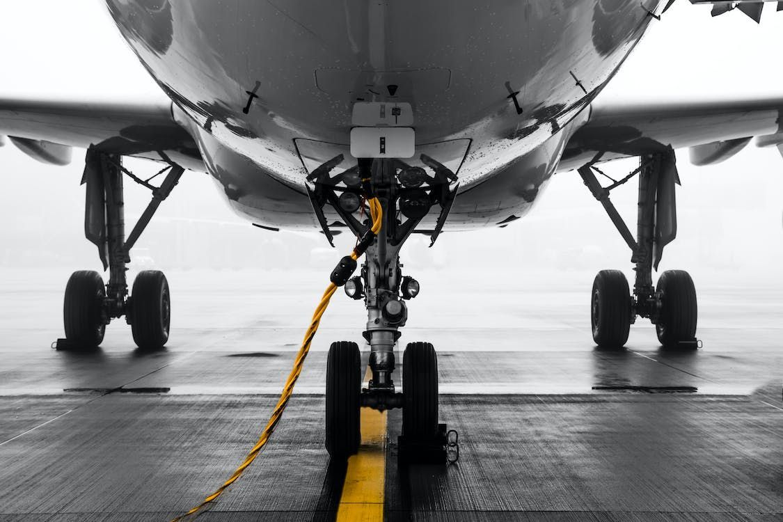Airplane nose gear on wet tarmac, with a yellow cable attached under the fuselage.