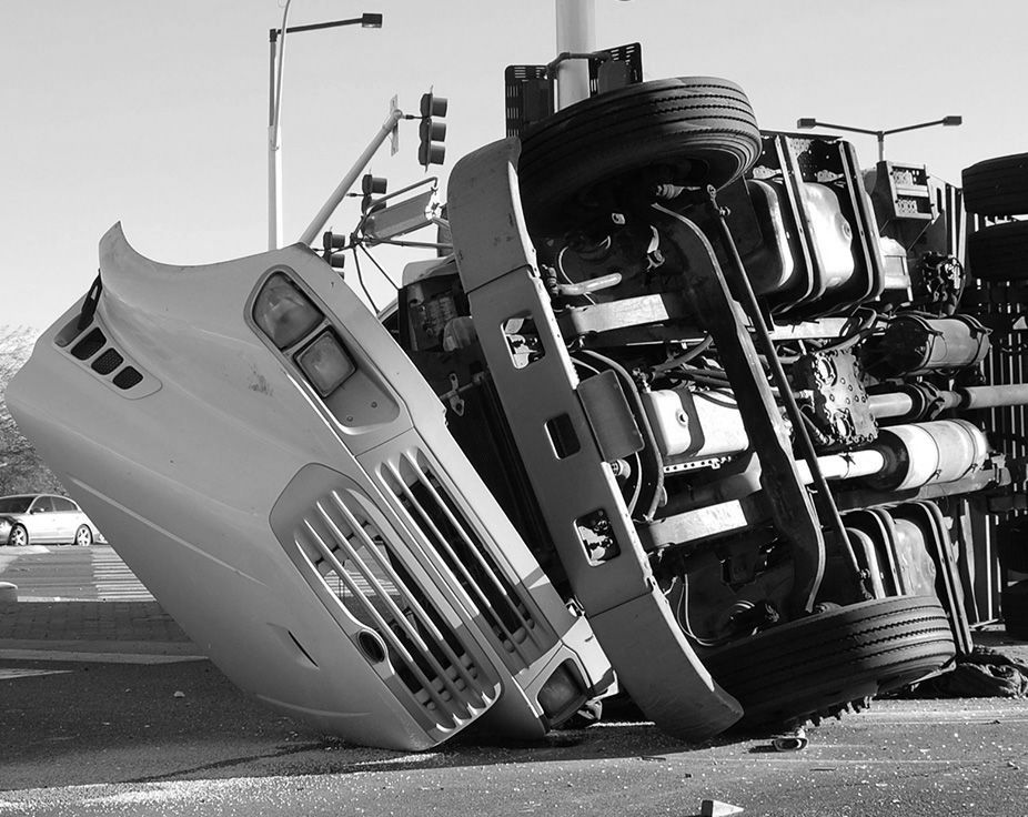 Overturned bus on its side after a crash, blocking a road in black and white.