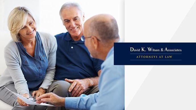 Three people meeting in a bright office, with “David K. Wilson & Associates: Attorneys at Law” on the wall.