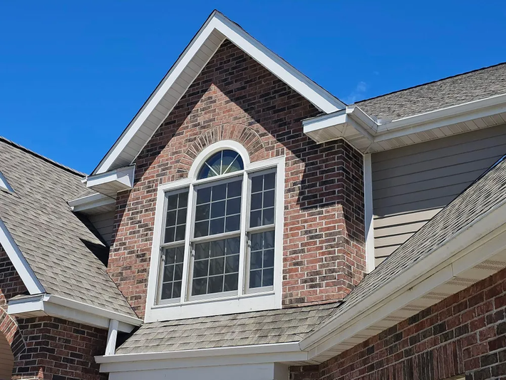 Brick house with a large window and gable roof against a blue sky.