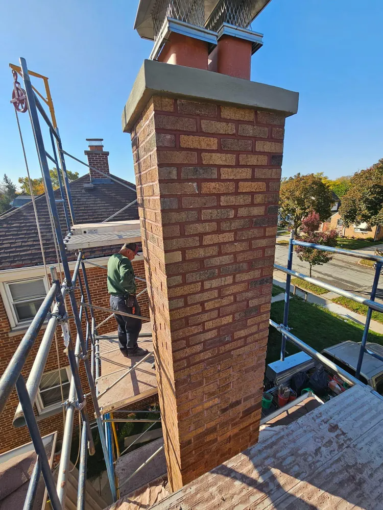 Brick chimney being worked on by a person on scaffolding.