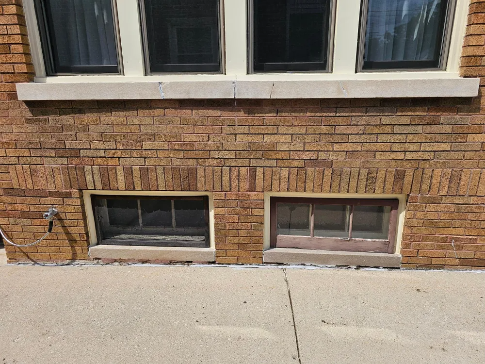 Brick building exterior with basement windows below upper windows; sidewalk in foreground.