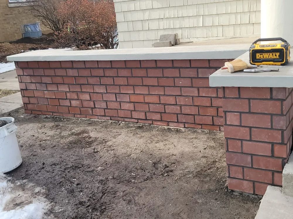 Red brick wall with concrete cap and column; a DeWalt speaker sits atop it.