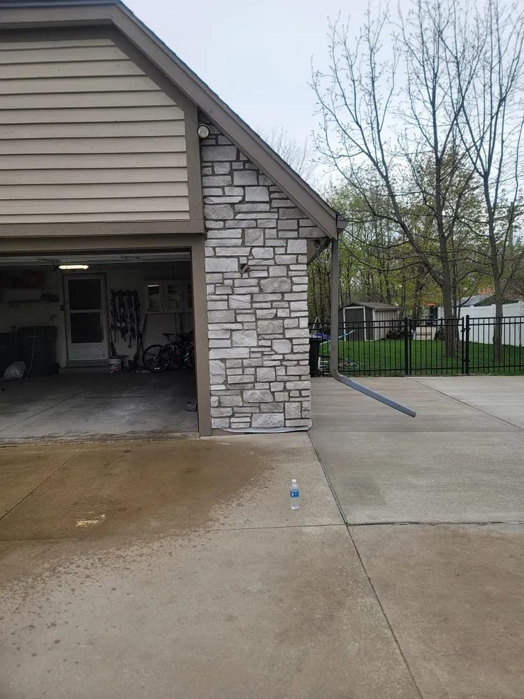 Garage exterior with stone siding and tan siding, wet driveway.