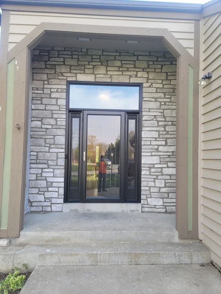 Front entrance with stone facade, black door and sidelights, concrete steps.