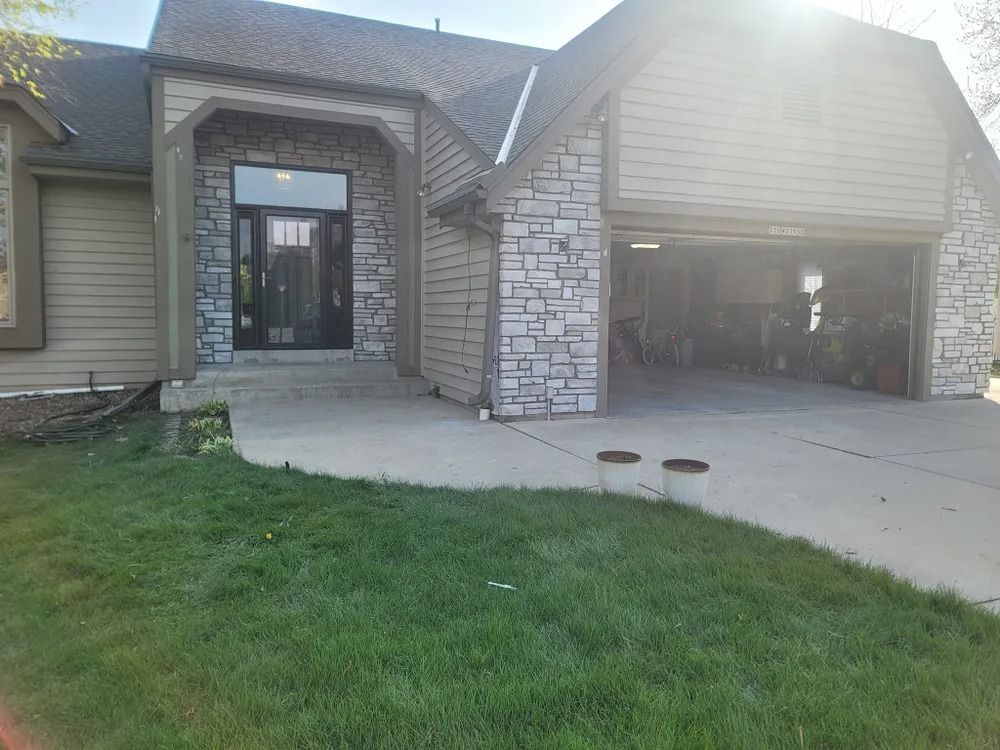 House exterior with stone accents, a concrete driveway, and open garage. Green grass in foreground.