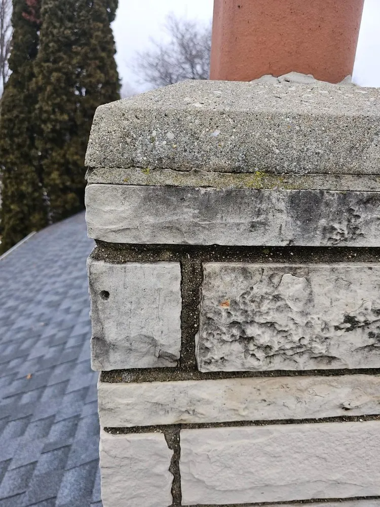 Close-up of a weathered stone chimney against a cloudy sky. Gray and white stones show wear and tear.