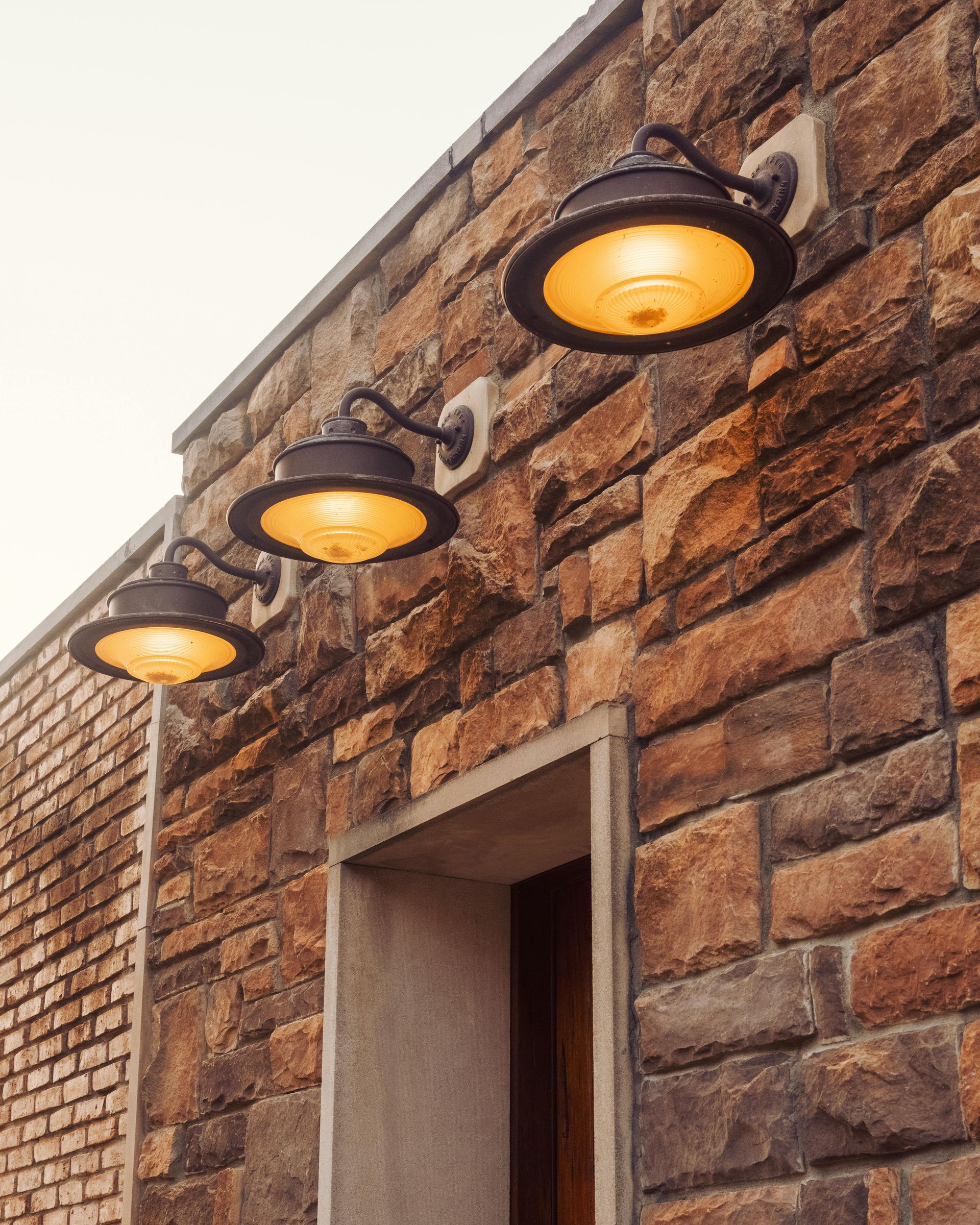 Three amber wall lanterns on a stone exterior above a doorway