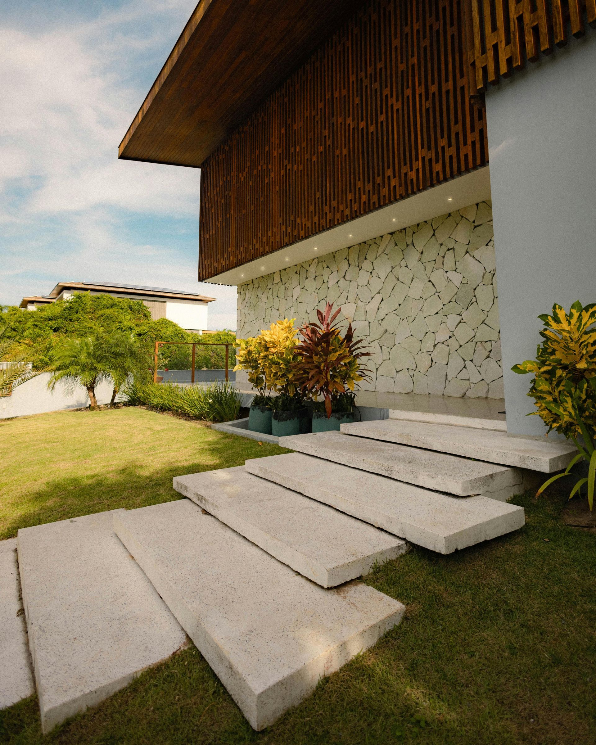 Modern house exterior with stone steps, green lawn, and wooden overhang