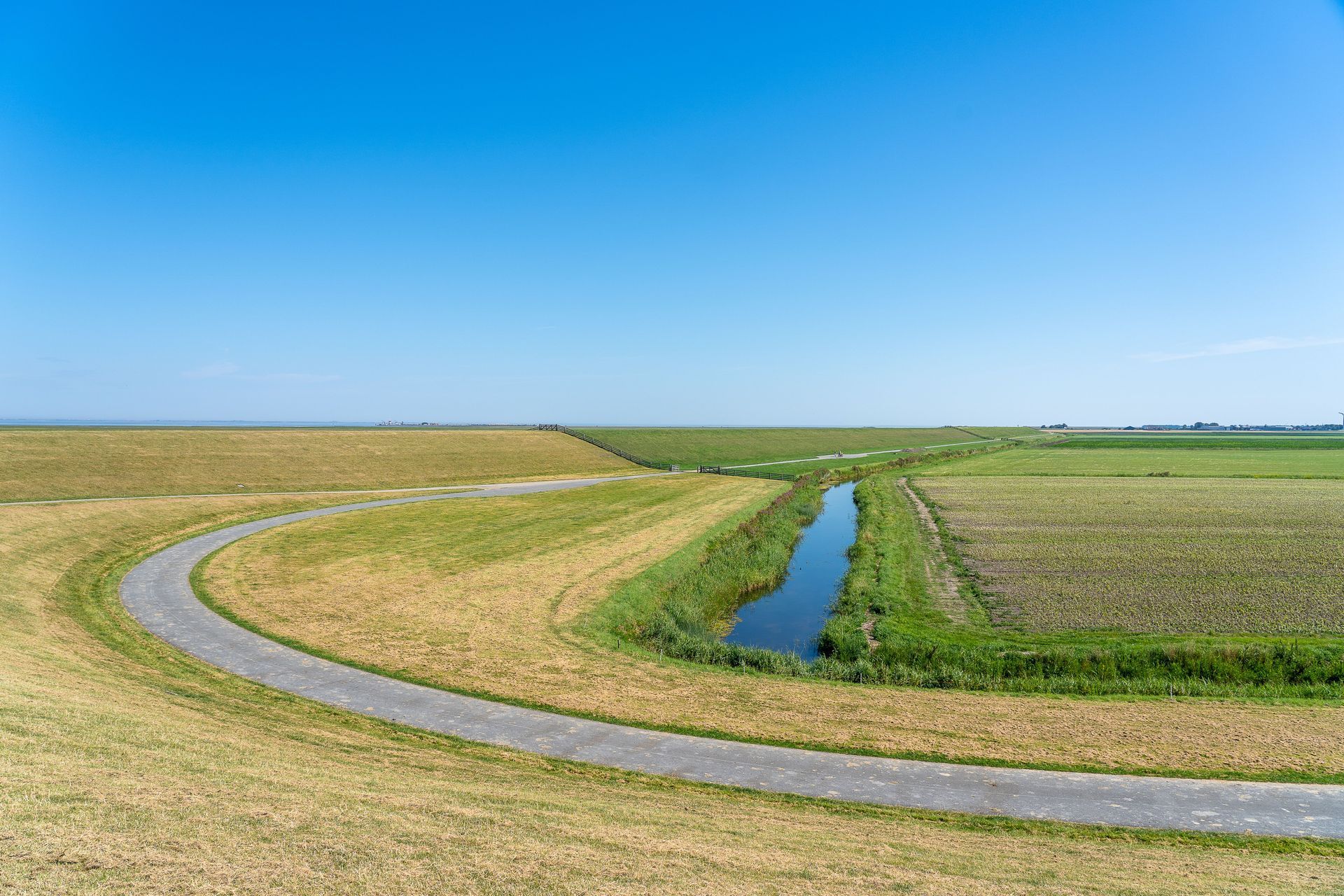 Curving rural road beside a narrow irrigation canal in flat farmland under a clear blue sky