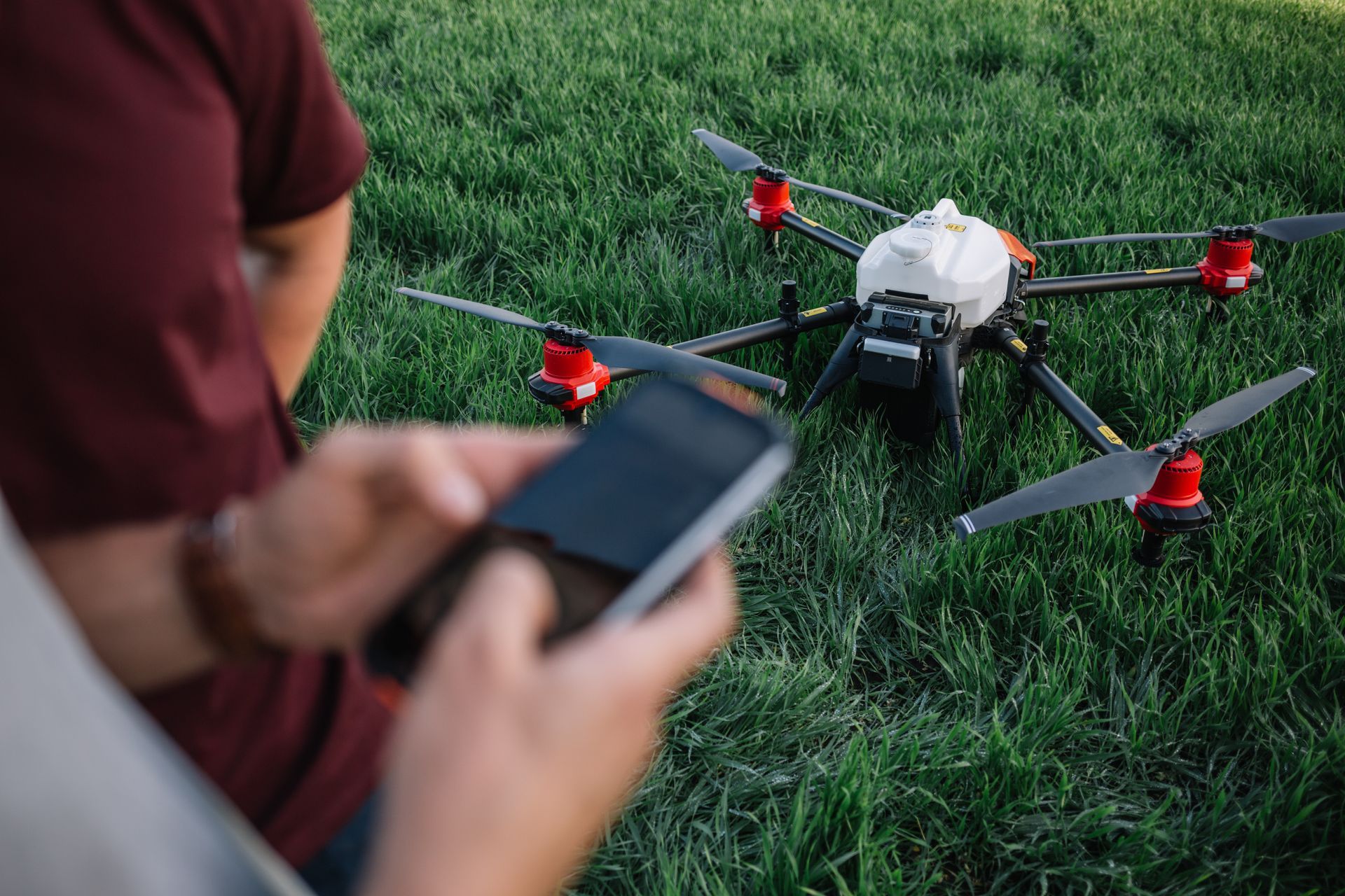 Person using a smartphone to control a quadcopter drone on grass