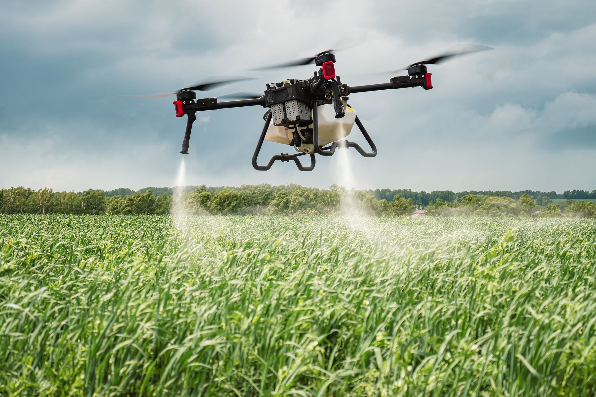 Drone spraying crops in a green field under a cloudy sky