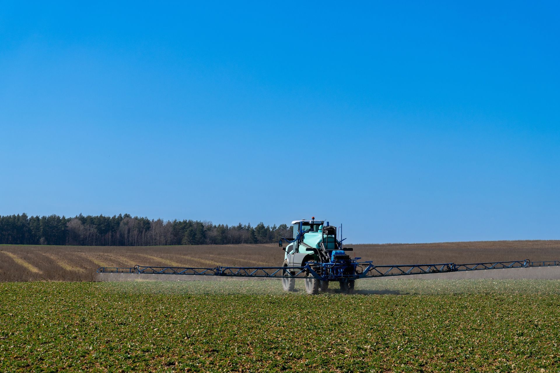 Tractor spraying a field under a clear blue sky