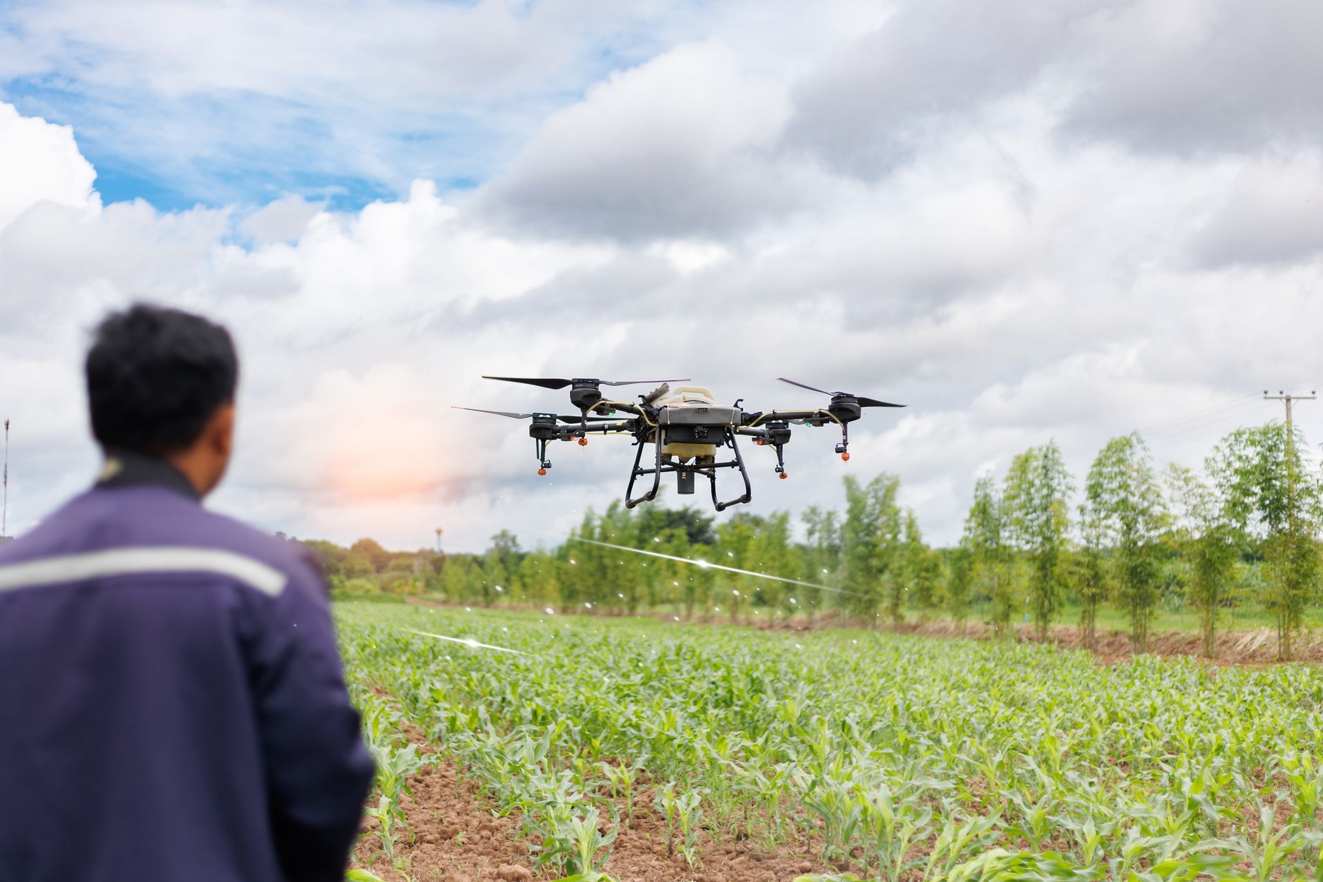 Drone spraying crops in a green field while a person watches from the foreground