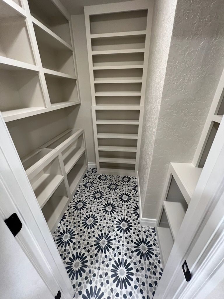 Walk-in pantry with white shelves and patterned tile floor.