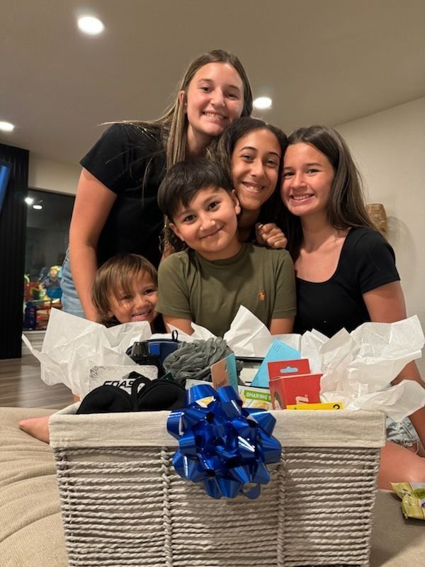 Five smiling people gather around a gift basket with a blue bow; indoors.