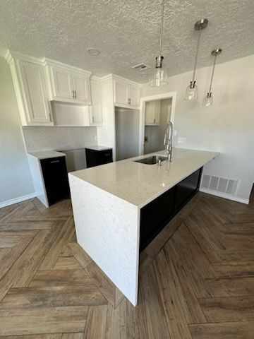 Modern kitchen with white cabinets, black island, light quartz countertop, and patterned wood floor.