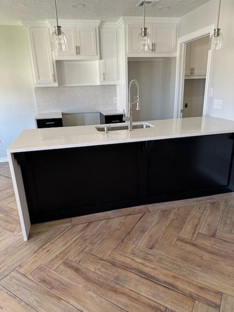 Modern kitchen with white cabinets, black island, light countertops, herringbone floor, and pendant lights.